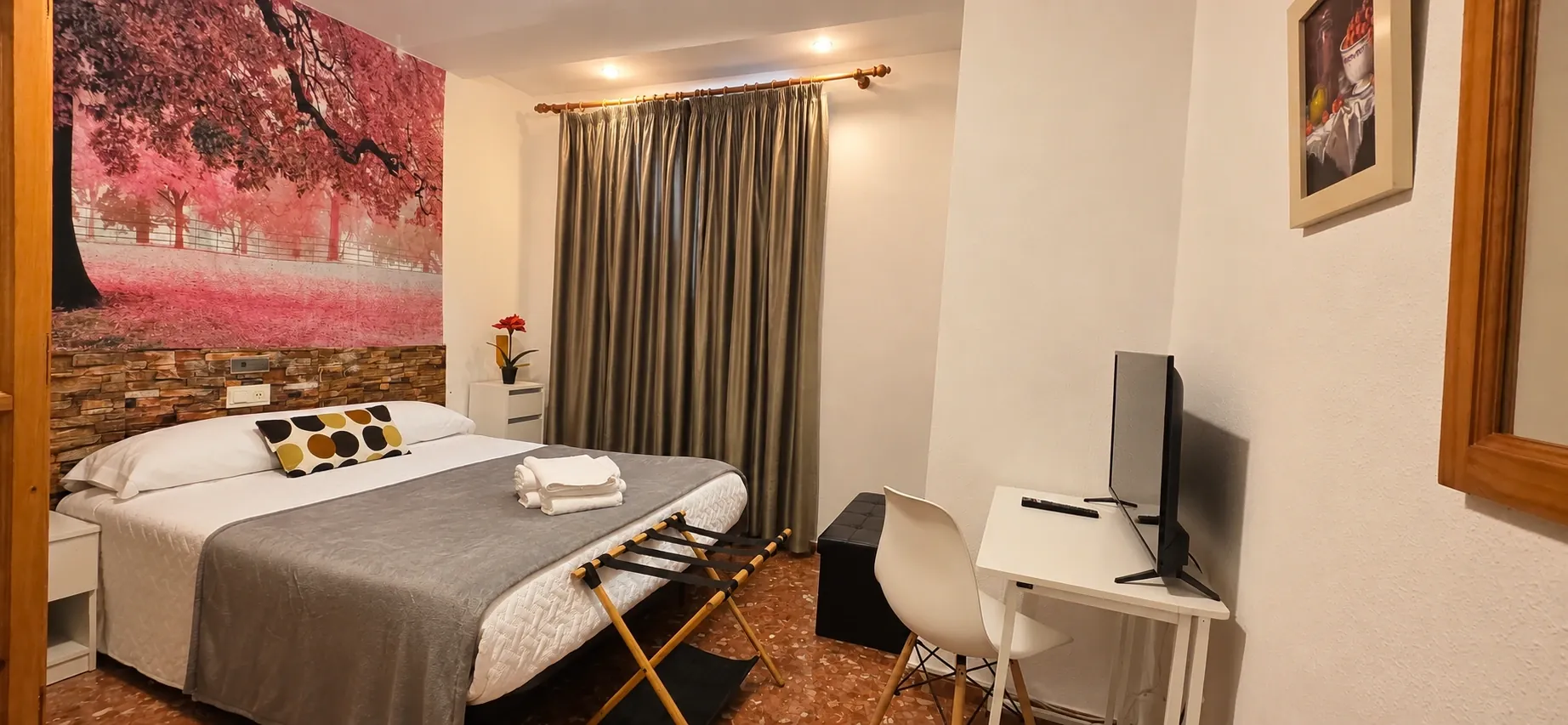 Double room with grey bedspread, desk and soft pink mural